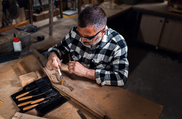 Carpenter sitting in his workshop restoring old piece of furniture with carving tool.