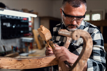 Carpenter standing in his workshop restoring old piece of furniture with hammer and chisel.