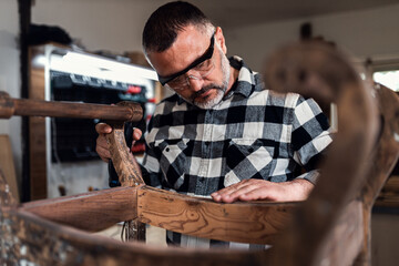 Carpenter standing in his workshop restoring old piece of furniture.