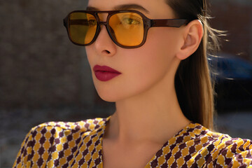 Outdoor fashion portrait of a  stylish young woman with sleek hair and bold red lips wearing...