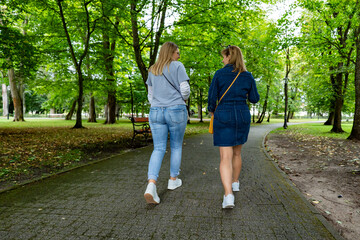 Obraz premium Two beautiful mature women walking in city park. Back view