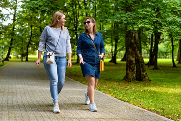 Fototapeta premium Two happy mature women walking in city park. Meeting of friends in park. Front view