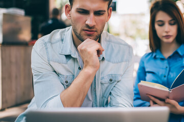 Fototapeta premium Focused man watching tablet and woman reading book in cafe