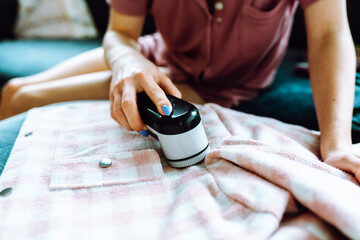 woman takes care of clothes at home, cuts off lint with tool