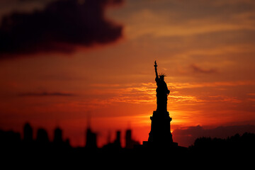 Silhouette of Statue Liberty against vibrant orange sunset sky, showcasing freedom and hope, iconic New York City landmark