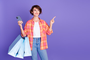 Photo of nice young girl phone bags direct finger empty space wear shirt isolated on violet color...