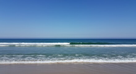 Ocean waves crashing on sandy beach under a clear blue sky.