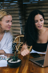 Serious caucasian females enjoying watching online video on laptop computer together on free time, smart women colleagues checking news from blog social network planning business organization