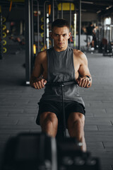Vertical photo of a focused, fit man working out on a rowing machine in a modern gym. Athletic...