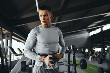 A professional bodybuilder adjusts his leather gym protection belt in a modern gym while looking away, focusing on safety and performance during an intense workout session.