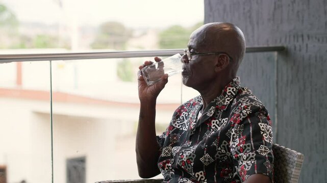 Elderly African man drinks a glass of water, hydrates for proper body function, healthy living during retirement.