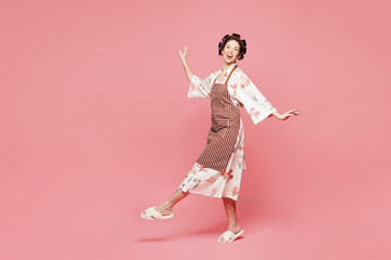 Full body side view young smiling happy housewife housekeeper chef cook baker woman wear brown apron dance walk go isolated on pastel light pink color background studio portrait. Cooking food concept.