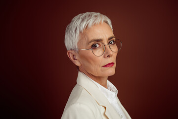 Elegant mature businesswoman with short white hair in formal attire posing confidently against a...