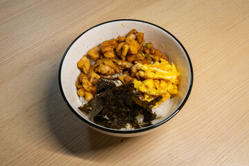 A bowl of rice topped with chicken, egg, and seaweed.