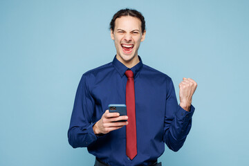 Young rich employee business man corporate lawyer wear classic formal shirt red tie work in office hold in hand use mobile cell phone do winner gesture isolated on plain pastel light blue background.