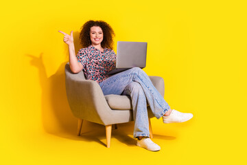 Confident young woman with curly brown hair using a laptop and making a pointing gesture in a...