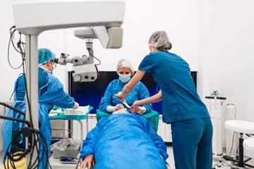 Skilled female surgeon and his medical team performs precise eye surgery on an elderly patient,...