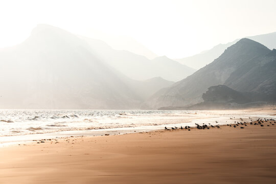 Friedliche K&uuml;stenszene mit sanften Wellen und nebelverhangenen Bergen im Oman Salalah