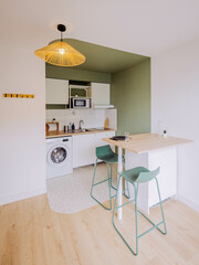 Cuisine moderne équipée avec coin repas et tabourets verts dans un appartement clair.