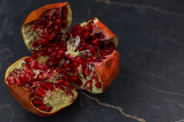 A vibrant and juicy pomegranate is split open, revealing its succulent red seeds against a dark...