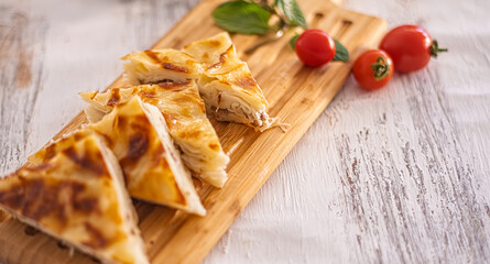 Close-up shot features sliced Turkish Börek. Flaky pastry arranged on wooden cutting board. Garnished with cherry tomatoes and mint leaves. Selective focus.