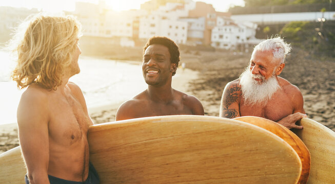 Multigenerational surfer friends having fun on the beach after surf session - Summer lifestyle, travel and extreme sport concept - Main focus on african man face