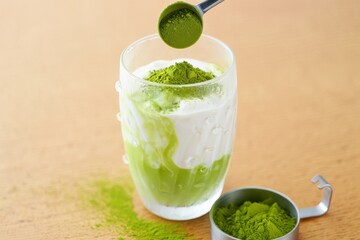 Making iced matcha latte in a tall glass with ice by adding matcha tea to milk