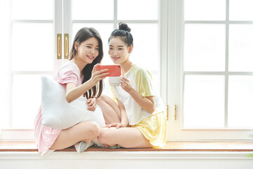 Obraz premium Young Women Friends Taking Selfie Indoors with Coffee by Window
