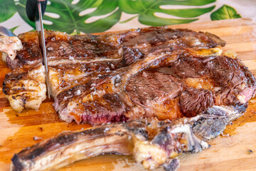 slicing a perfectly cooked chuletón steak with knife and fork close view of a grilled steak on a wooden board being cut