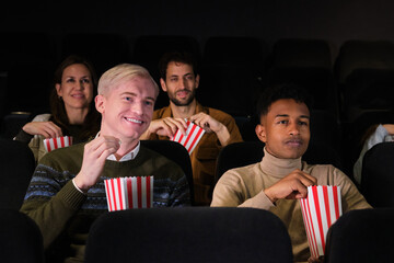 Group of friends watching a movie and eating popcorn at the cinema