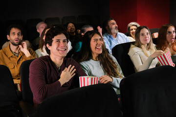 Diverse group of friends having fun watching a comedy movie at the cinema, laughing and eating popcorn