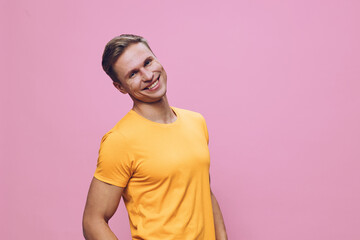 Smiling young man wearing bright orange t-shirt look camera standing on pink background cheerful...