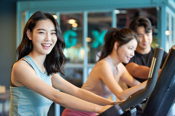 Young Asian Women and Man Exercising Together on Treadmills at Gym