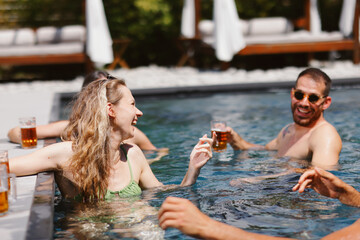 Group of friends laughing and enjoying refreshing beers in a swimming pool on a sunny day