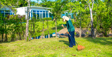 A janitor cleans the lawn area from leaves and mown grass. Hotel cleaning service.