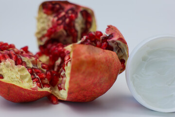 A vibrant pomegranate revealing juicy seeds beside a container of cream, perfect for health and...