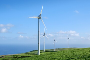 Modern wind turbines on the verdant hills of Serra do Cume with a sweeping vista of Terceira Island. The image captures the renewable energy technology with the natural beauty of the Azores landscape