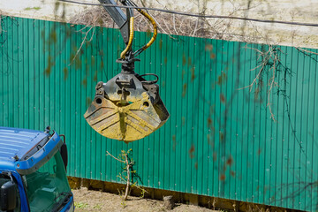 An excavator bucket with a grapple filled with sand against the backdrop of a construction fence,...