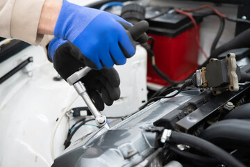 A mechanic in gloves using a wrench to tighten a spark plug in an engine during a vehicle repair session inside the workshop.