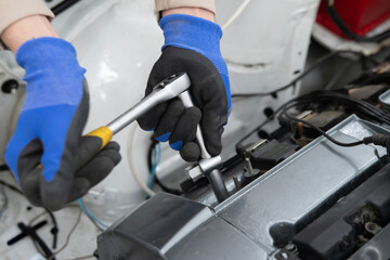 A mechanic in gloves using a wrench to tighten a spark plug in an engine during a vehicle repair...