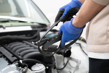A skilled car mechanic carefully holds a new timing belt while preparing to install it in an engine...