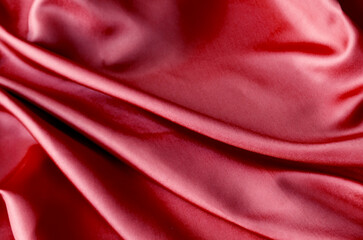 Vibrant dark red fabric draped in soft, smooth waves with a glossy finish. Suitable for design and...