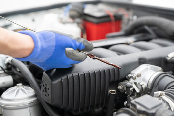 Fototapeta premium Mechanic uses a dipstick to check engine oil levels under the hood, ensuring vehicle operates efficiently and safely during maintenance checks.