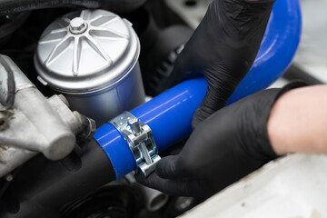 A car mechanic uses a metal clamp to secure a blue hose while performing maintenance in an auto...