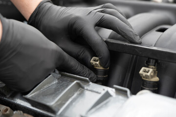 Mechanic with gloves carefully installs a fuel injector in a vehicle engine at a workshop,...