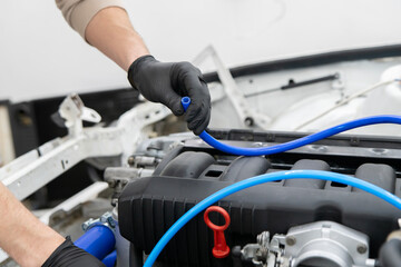 Mechanic works on car engine, carefully installing a blue fuel hose to enhance vehicle performance...