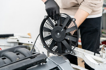 Technician handles an electronic fan while installing it in the engine compartment for proper...