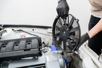 Technician handles an electronic fan while installing it in the engine compartment for proper...