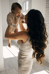 Loving mother taking care of her newborn baby at home. Bright portrait of happy mother holding sleeping baby in her arms. Mother hugging her little baby. 