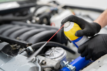 Using a car cleaner spray, a person applies it to engine parts in a garage to maintain vehicle...